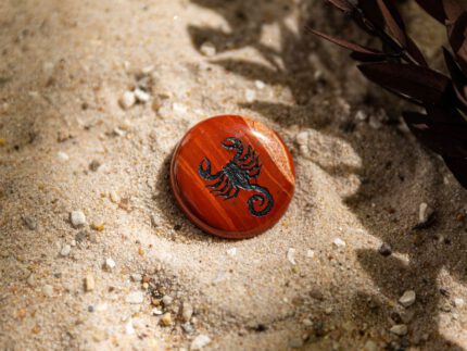 Stimmungsbild runder, rotbrauner Handschmeichler mit Sternzeichen Krebs-Motiv liegt auf Sand