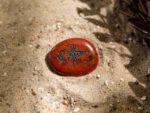 Ovaler, roter Taschenstein mit schwarzem Skorpion-Motiv liegt auf Sand