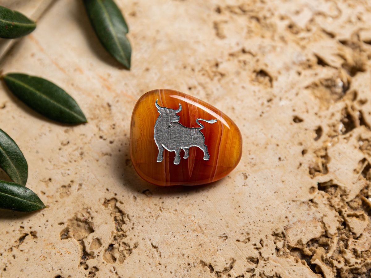 Orangener Taschenstein mit Stier-Motiv liegt auf Naturstein