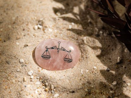 Zartrosa Taschenstein mit Waage-Motiv liegt auf Sand